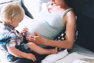pregnant mother and young son playing on the bed